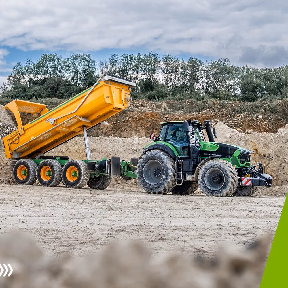 Green tractor with front weight bumper attached, pulling a yellow dump trailer unloading soil at a construction site