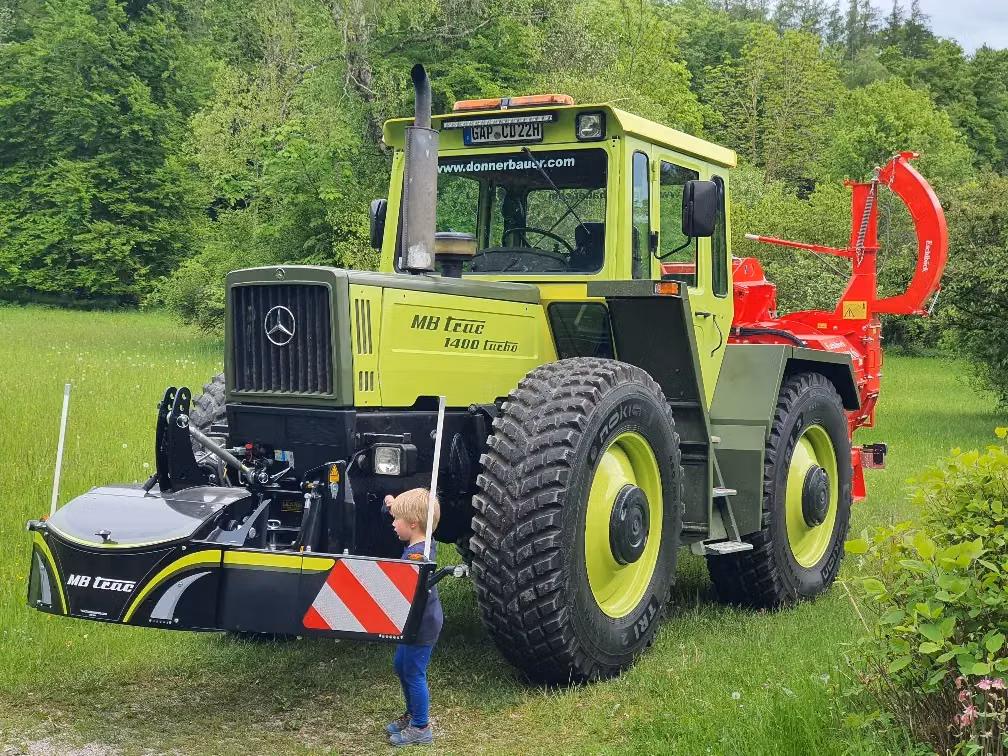 A child stands next to a tractor fitted with a large black front weight bumper featuring red and white stripes
