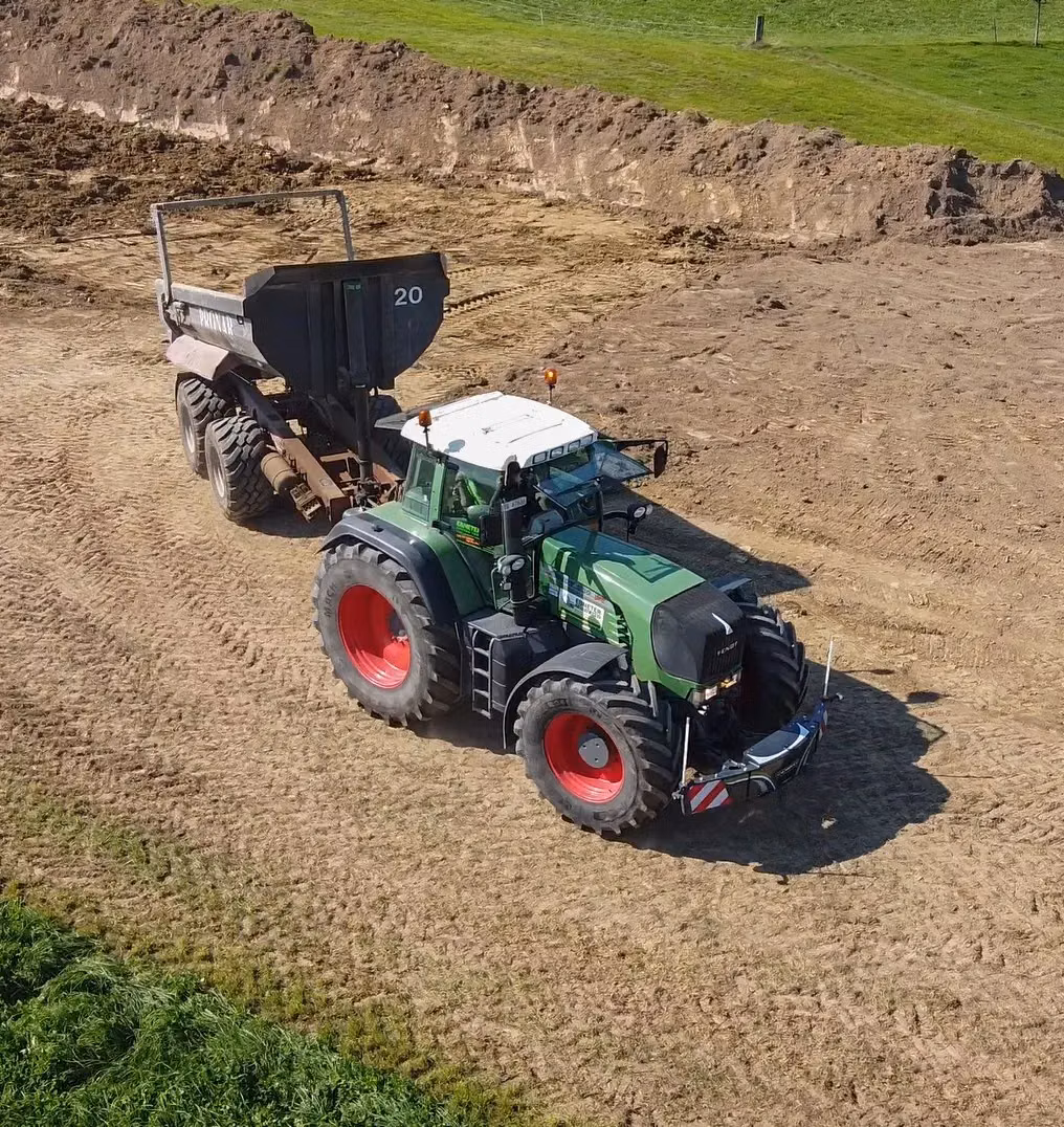 Green tractor with red wheels fitted with a front weight bumper, towing a trailer on a dirt field