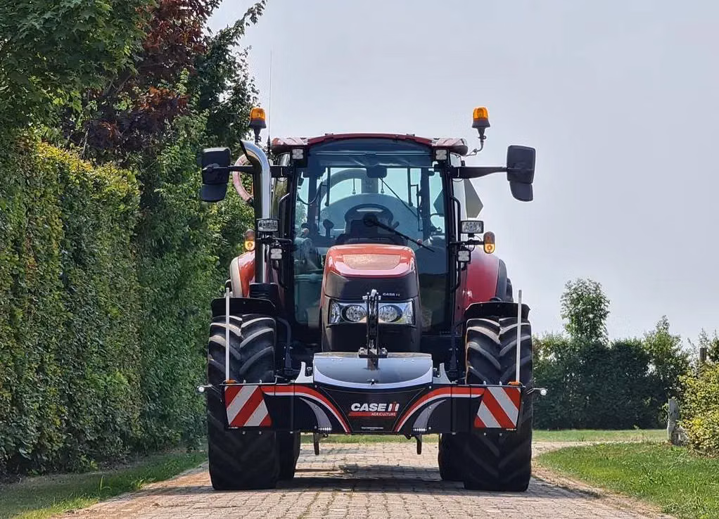 Red tractor with a front weight bumper featuring CASE IH branding and reflective safety markings on a paved path