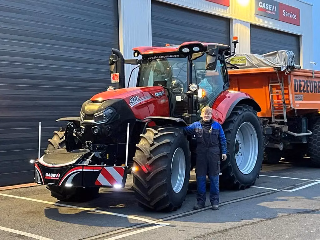 Person standing beside a red tractor fitted with a large black front weight bumper in a service yard