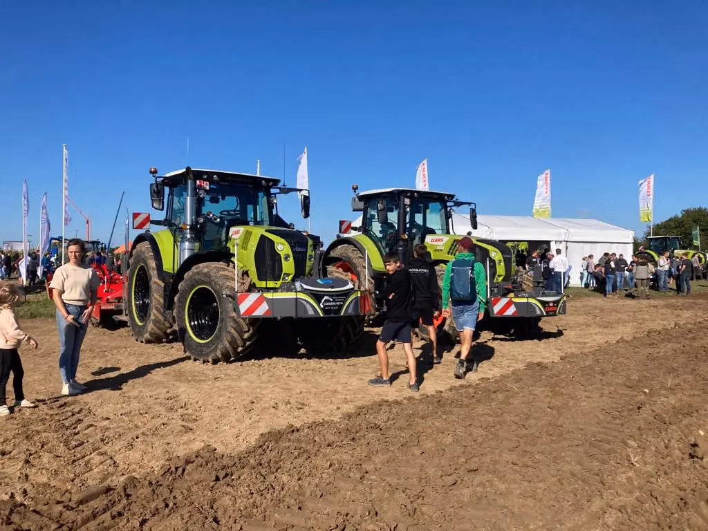 Two green tractors with front weight bumpers on display outdoors with people walking around on a sunny day