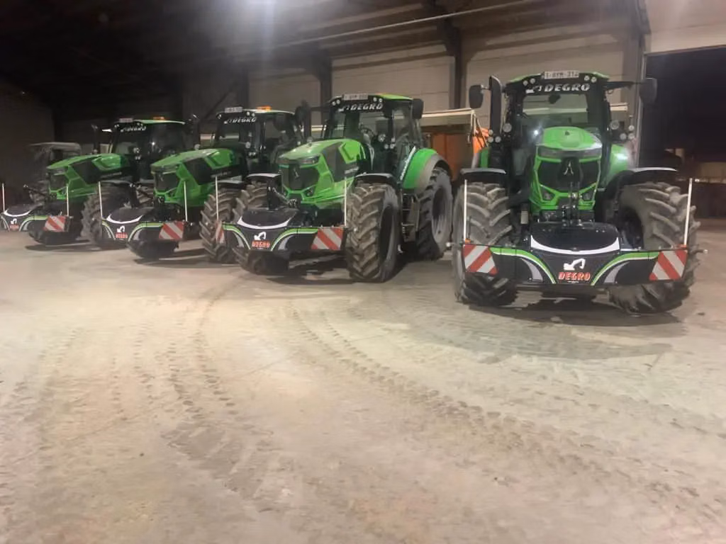 Four green tractors indoors, each equipped with front weight bumpers marked with red and white stripes and Degro logos