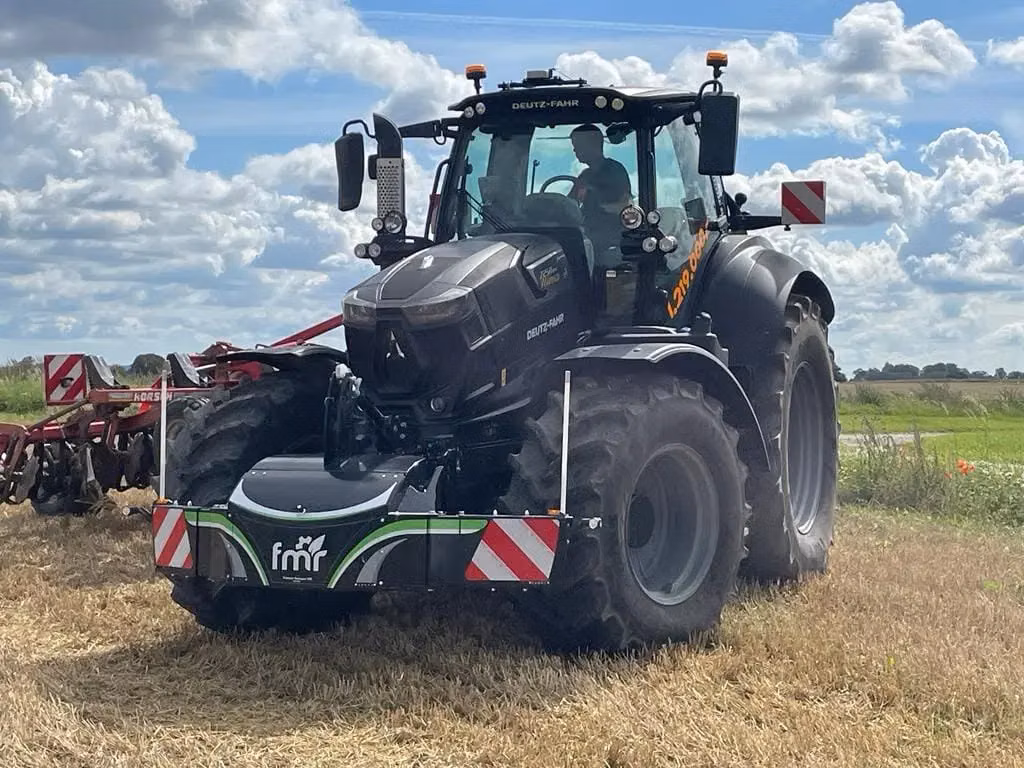 A tractor equipped with a large front weight bumper marked with reflective red and white stripes in a field