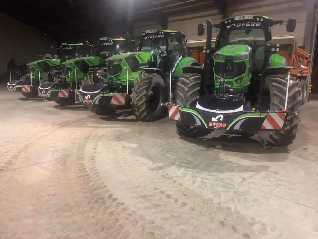 Four green tractors with large front weight bumpers labeled DE GRO parked indoors in a row