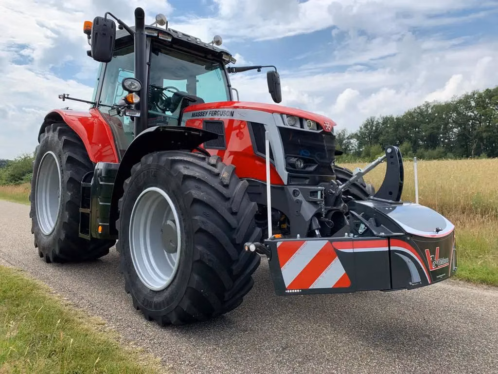 Red tractor with large tires shown on a rural road, featuring a mounted front weight bumper with reflective stripes