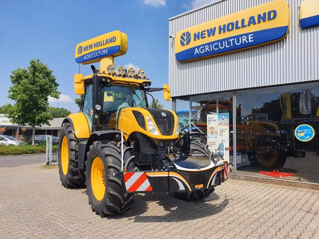 Yellow and black tractor with a large front weight bumper parked outside a New Holland Agriculture dealership