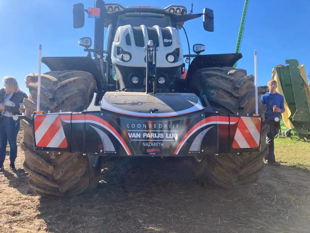 Large tractor with a mounted front weight bumper featuring storage space, LED lights and red-white safety stripes