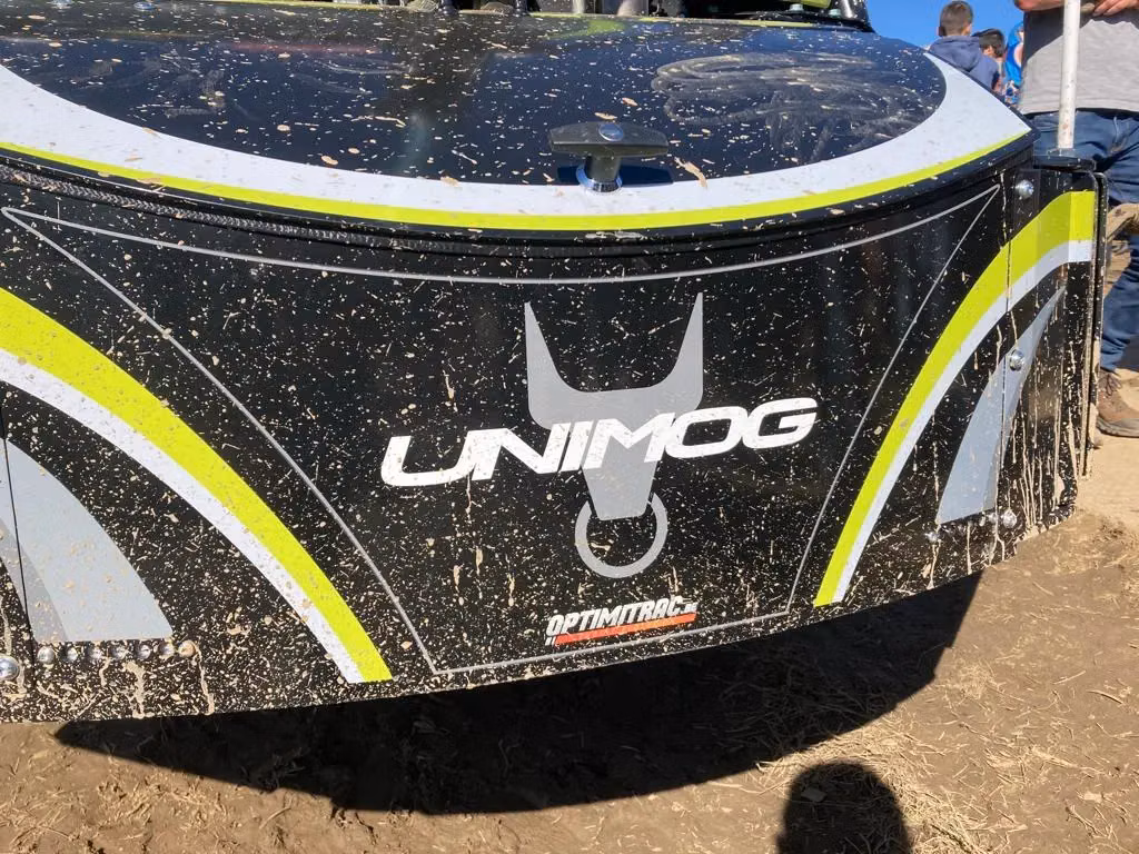 Black and yellow front weight bumper with the UNIMOG logo, splattered with mud, attached to a tractor