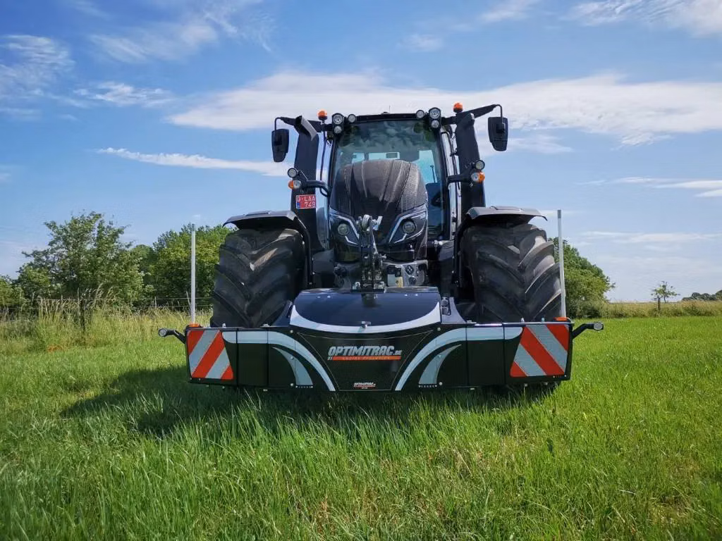 A tractor on grass equipped with a front weight bumper featuring safety stripes and LED lights