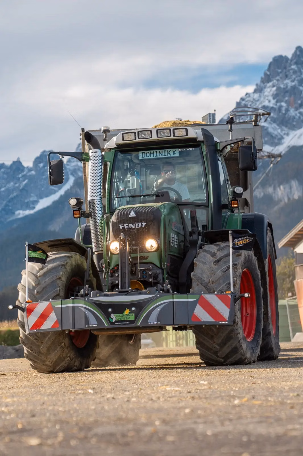 A tractor with a front weight bumper and safety markings is parked on a dirt surface with mountains in the background