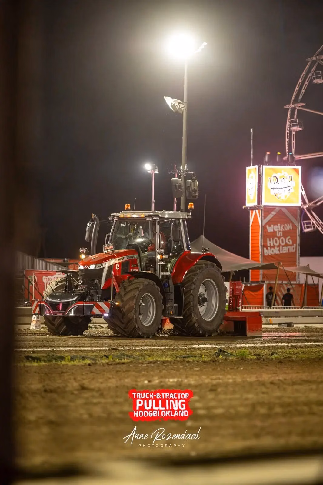 A red tractor with a front weight bumper is parked on a dirt track at night under bright lights