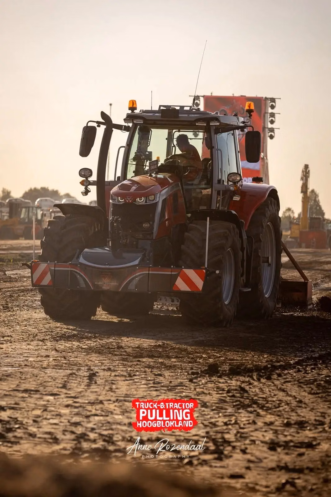 A red tractor with a front weight bumper drives on a dirt track at a tractor pulling event