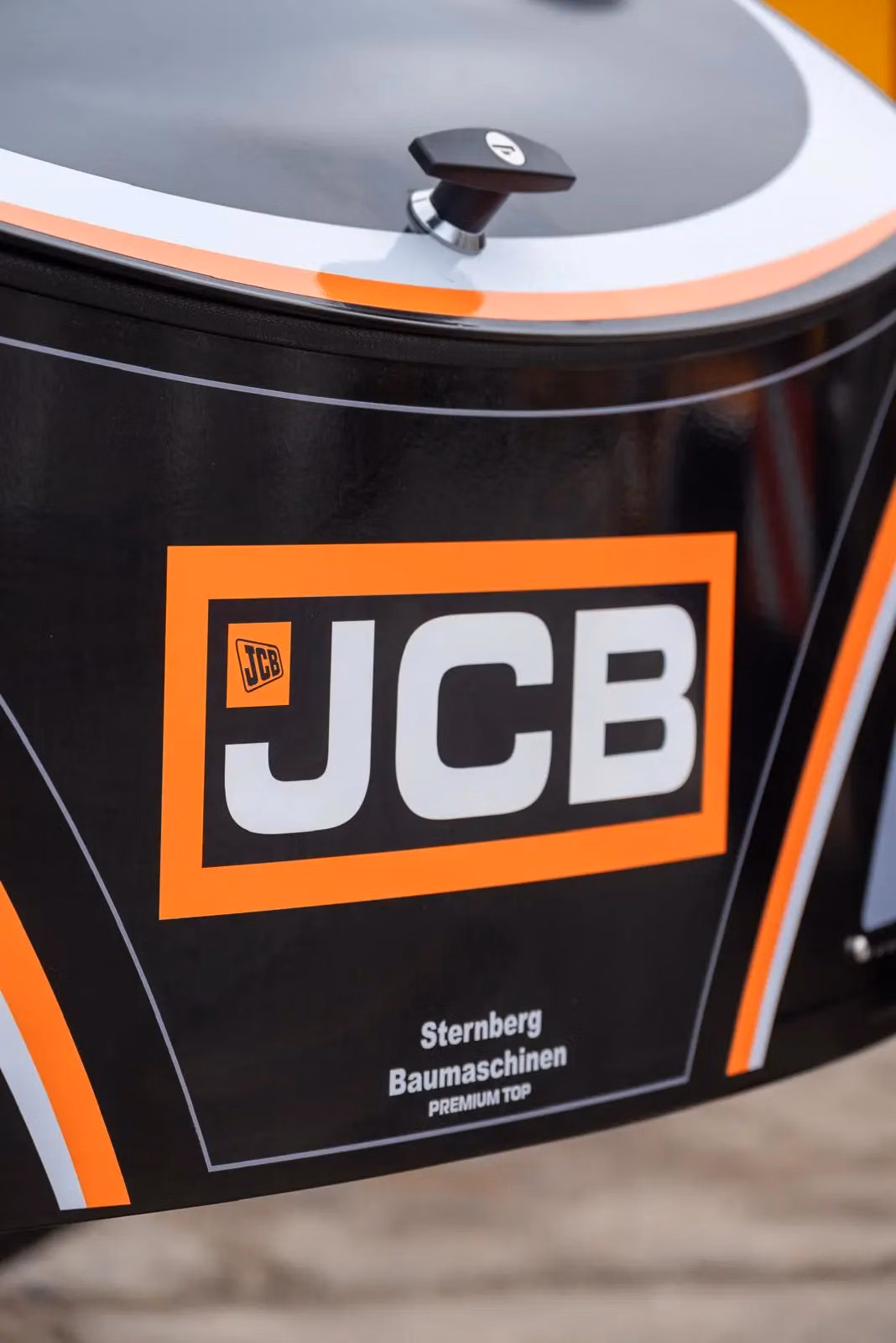 Close-up of a black front weight bumper with JCB branding, orange and white stripes, and a Sternberg Baumaschinen label