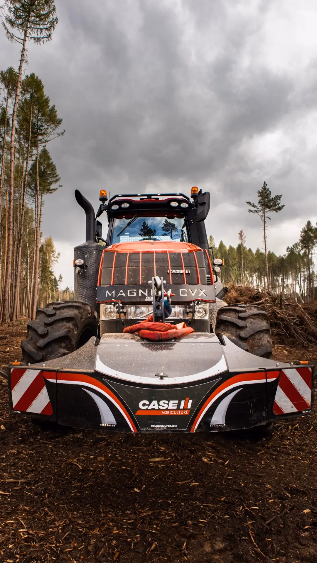 Front view of a Case IH tractor fitted with a black front weight bumper in a forest clearing under cloudy skies