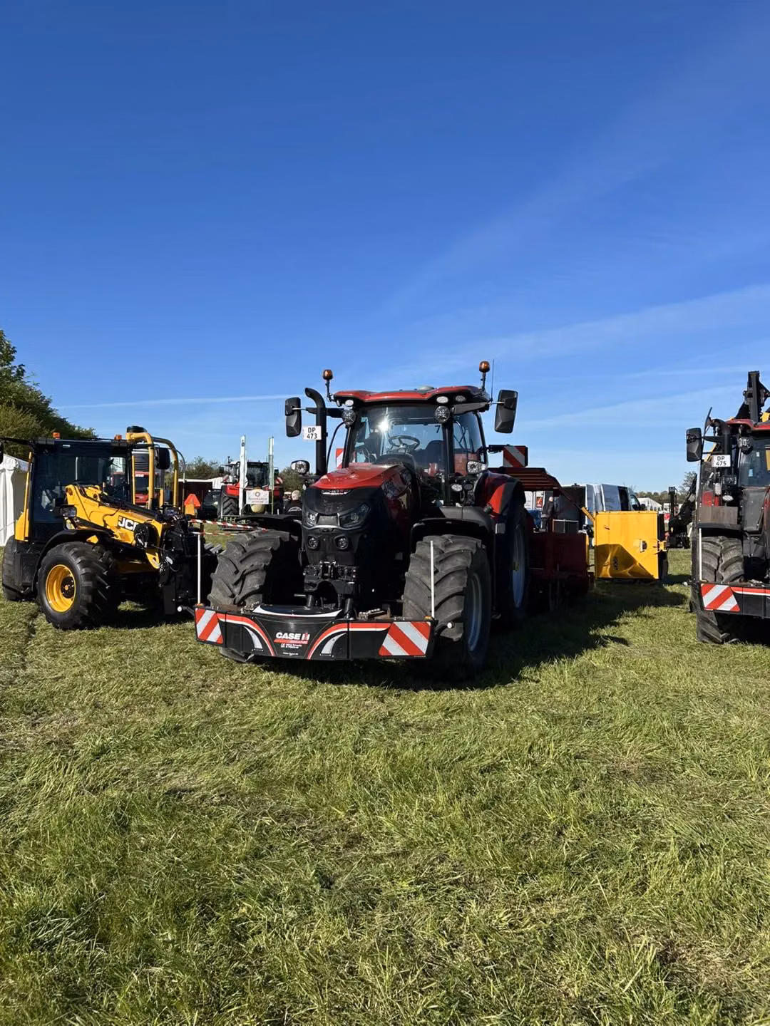 Red tractor with a front weight bumper labeled Case IH parked on grass between other machinery under a clear blue sky