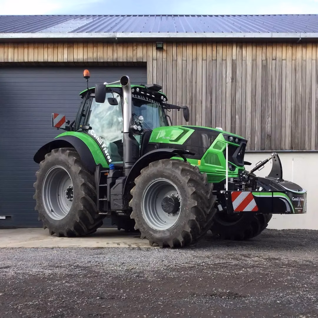 Green tractor with large tires is parked outside a building, fitted with a front weight bumper featuring safety stripes