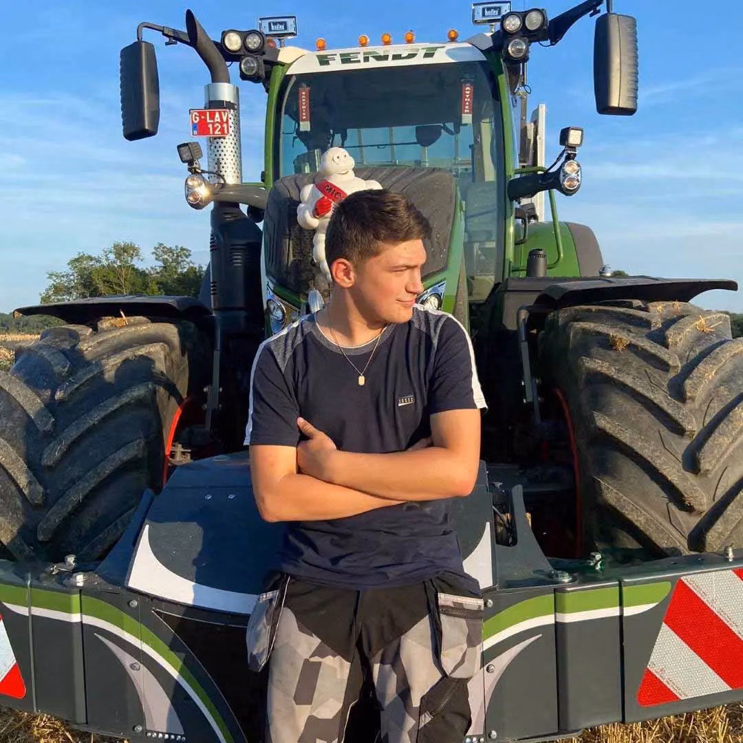 Young man with folded arms leans against a tractor front weight bumper with LED lights and striped markings
