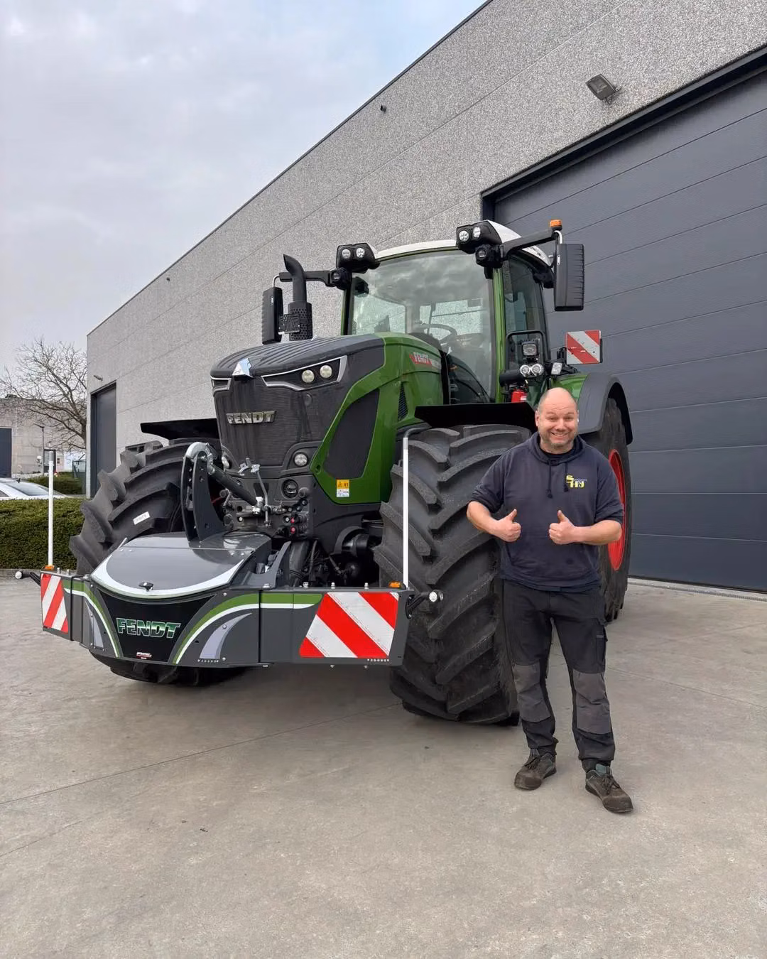 A man gives thumbs up beside a green tractor fitted with a large front weight bumper with safety markings