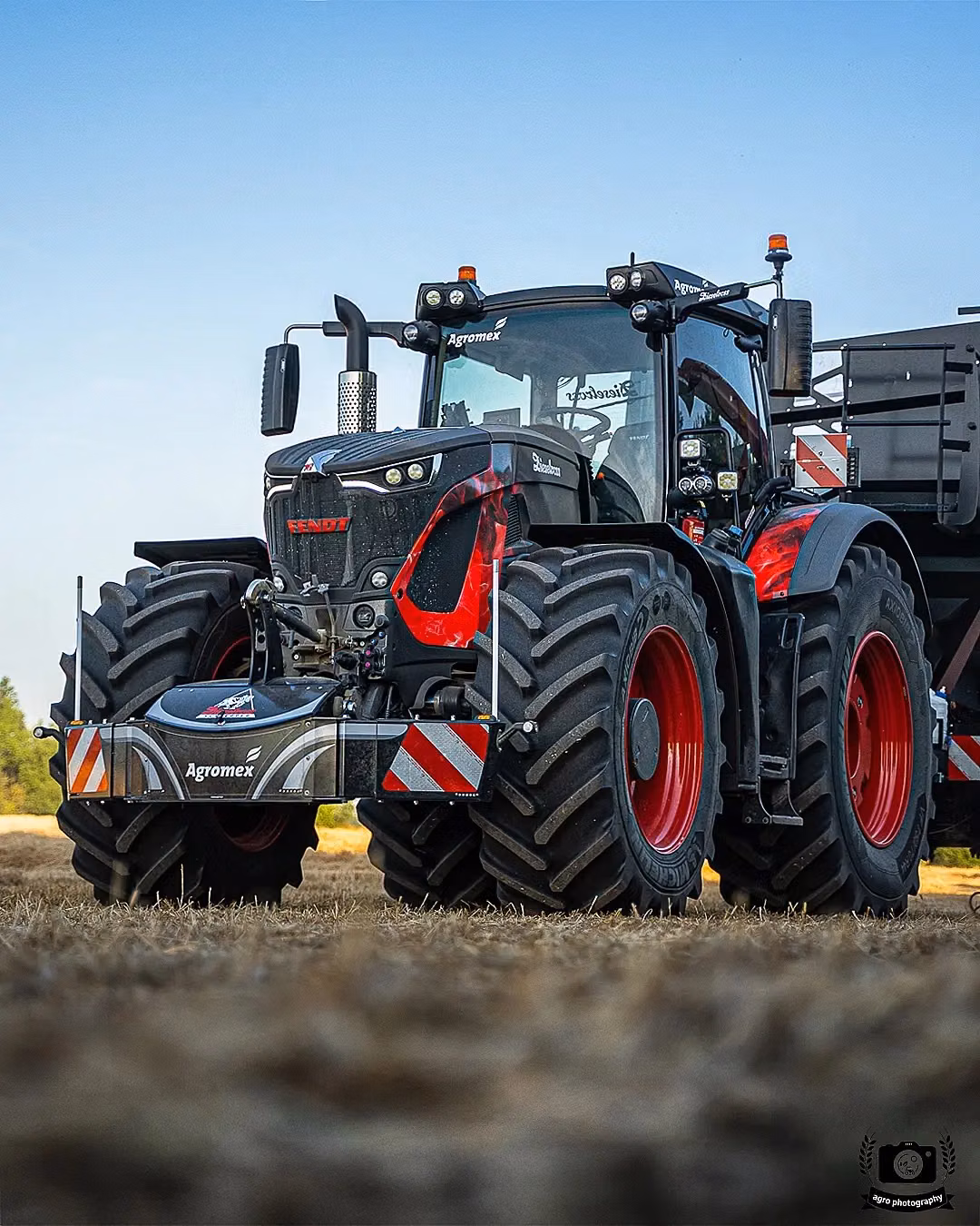 Large tractor with a front-mounted weight bumper featuring red and white safety stripes and integrated lights