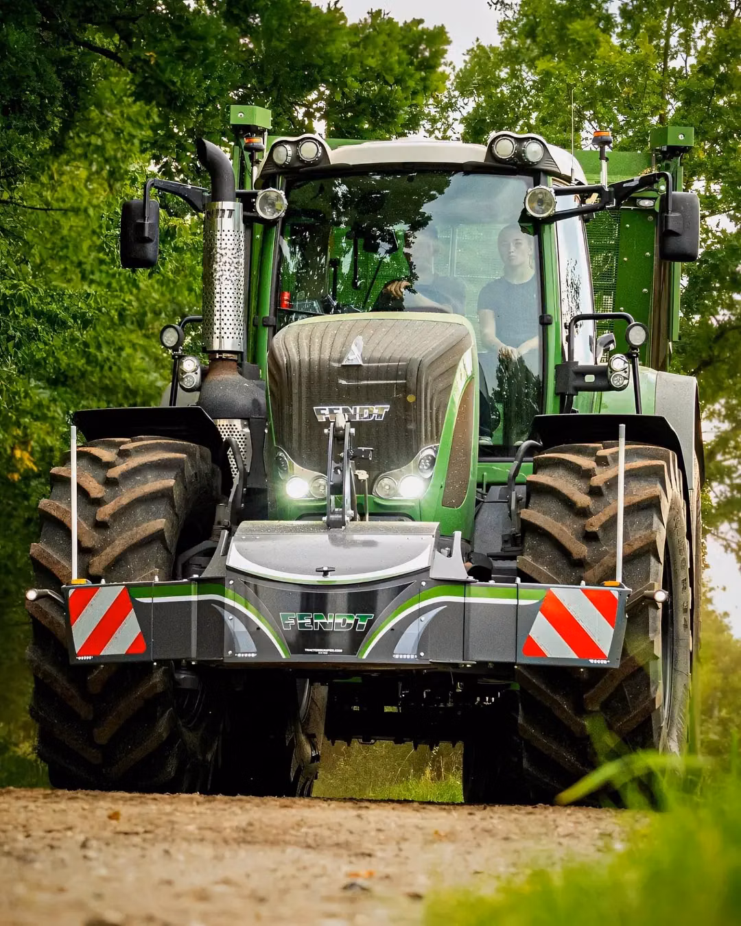 A green tractor with a Fendt front weight bumper featuring safety markings and integrated lights on a dirt path