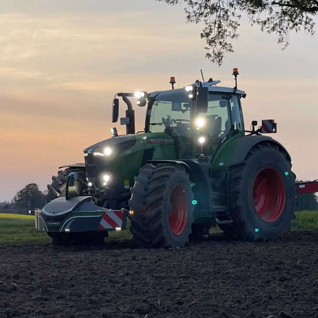 A tractor with large front weight bumper featuring lights and reflective safety markings in a field at dusk
