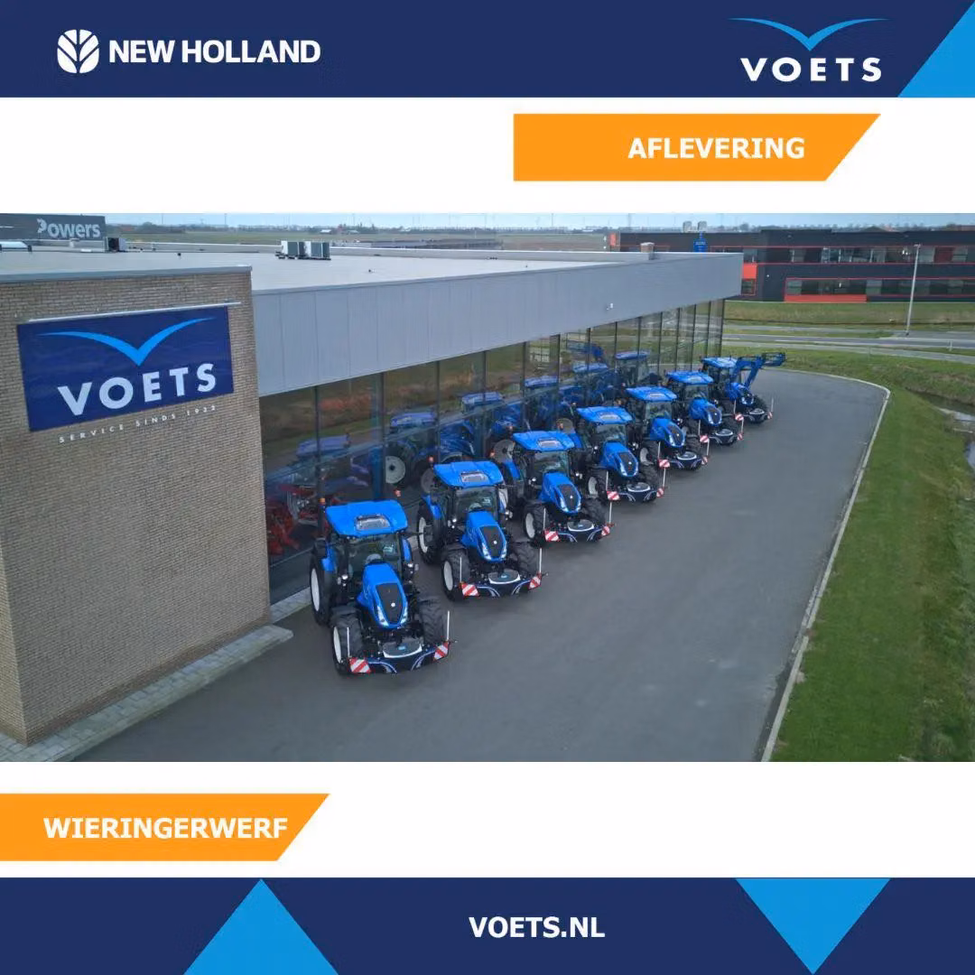 Row of blue tractors with front weight bumpers parked outside a building with large windows and a Voets sign