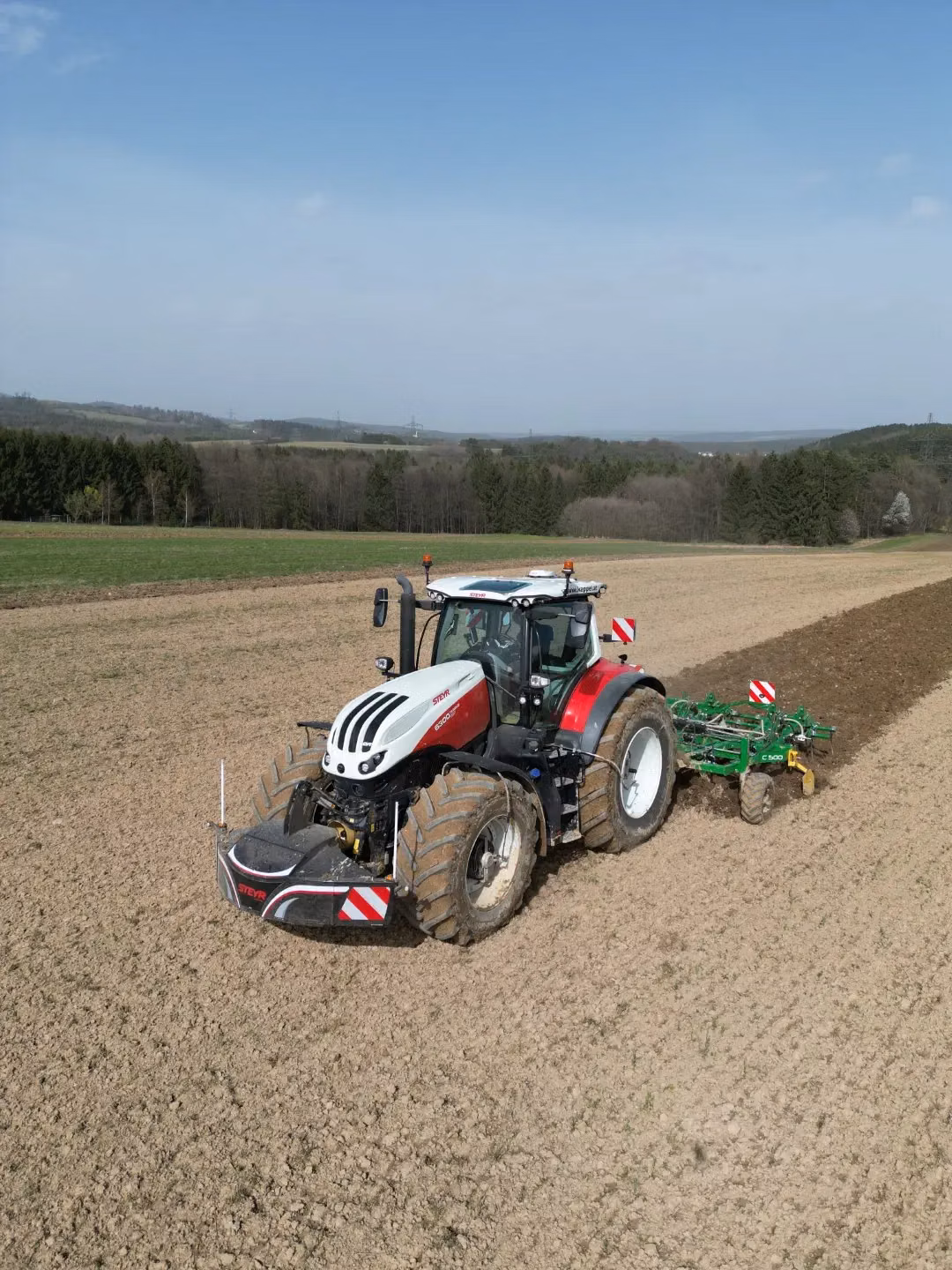 A red and white tractor with a front weight bumper attached works in a plowed field under a blue sky