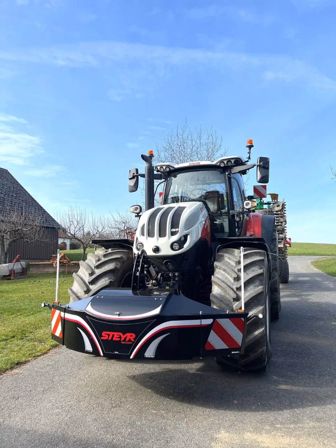 A large tractor with a black and red front weight bumper labeled STEYR parked on a paved driveway outdoors