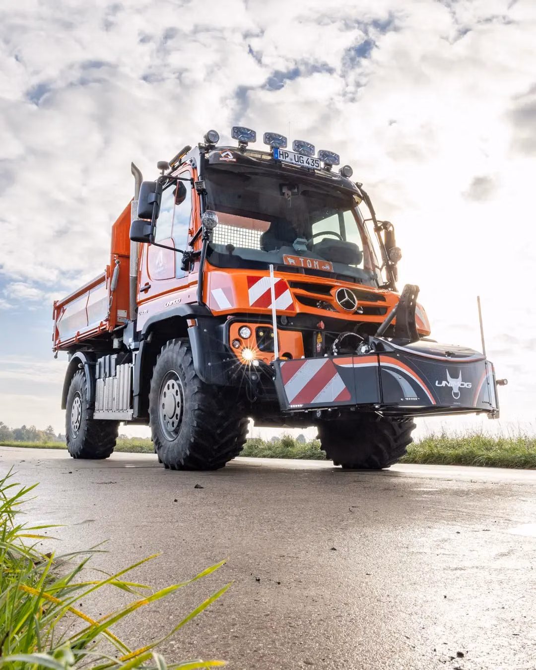 Orange utility vehicle with a front weight bumper featuring red and white safety stripes on a rural road