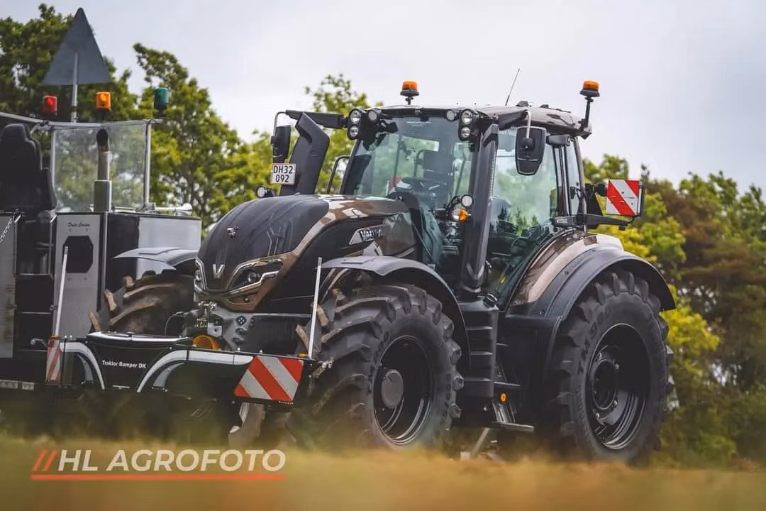 A tractor fitted with a front weight bumper featuring warning stripes and reflective markers on grass.