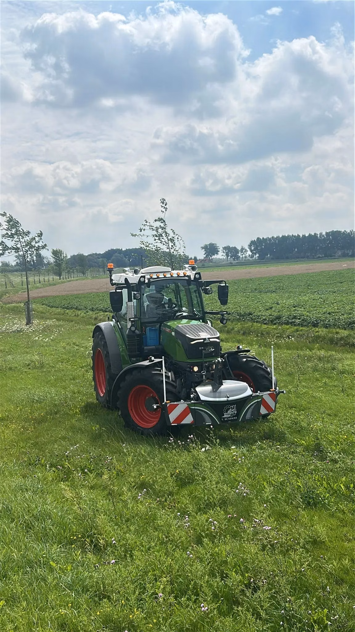 A green tractor in a grassy field fitted with a front bumper featuring lights and red and white safety markings