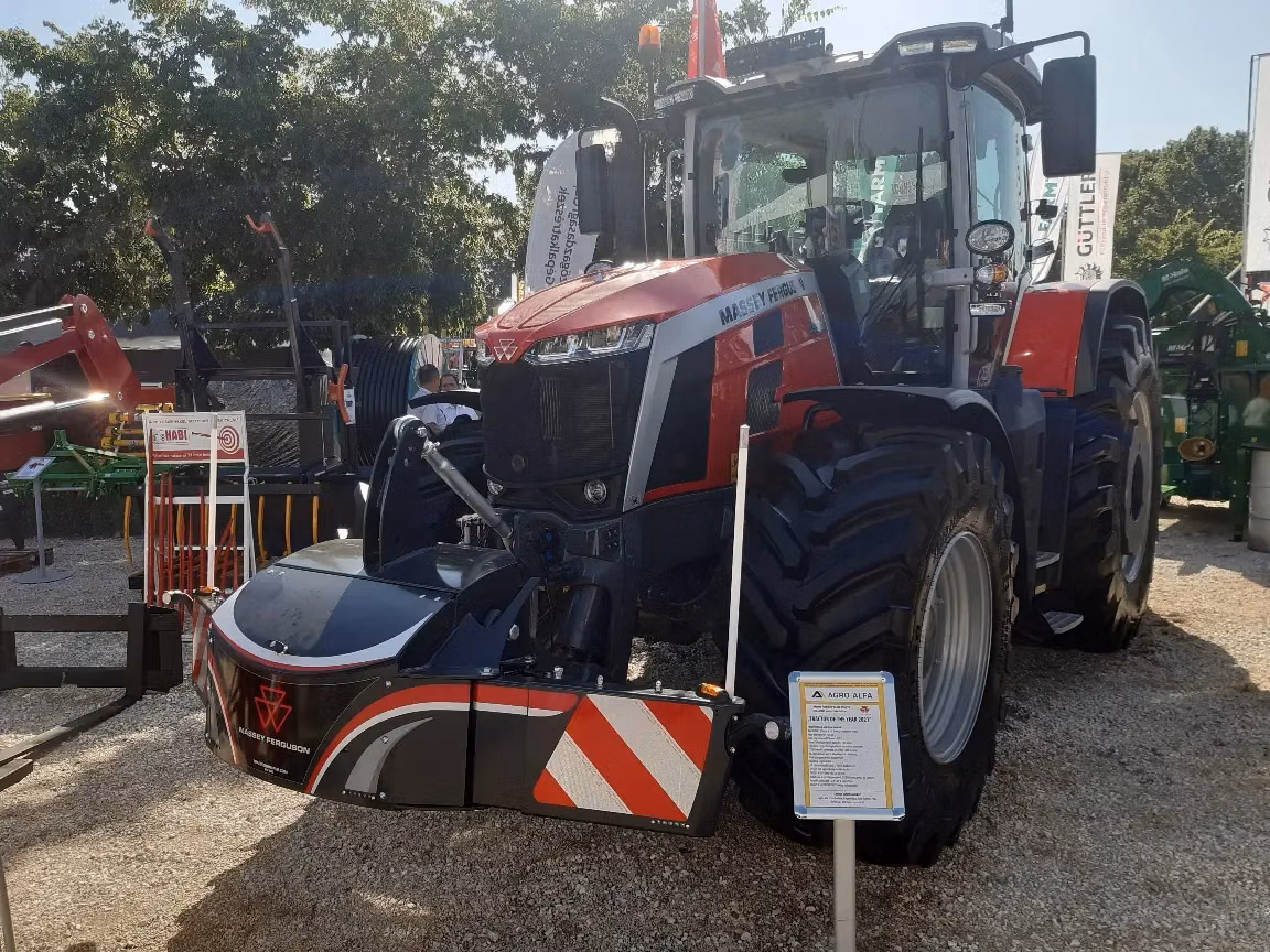 Red and black tractor with a Massey Ferguson branded front weight bumper displayed outdoors on gravel with informational