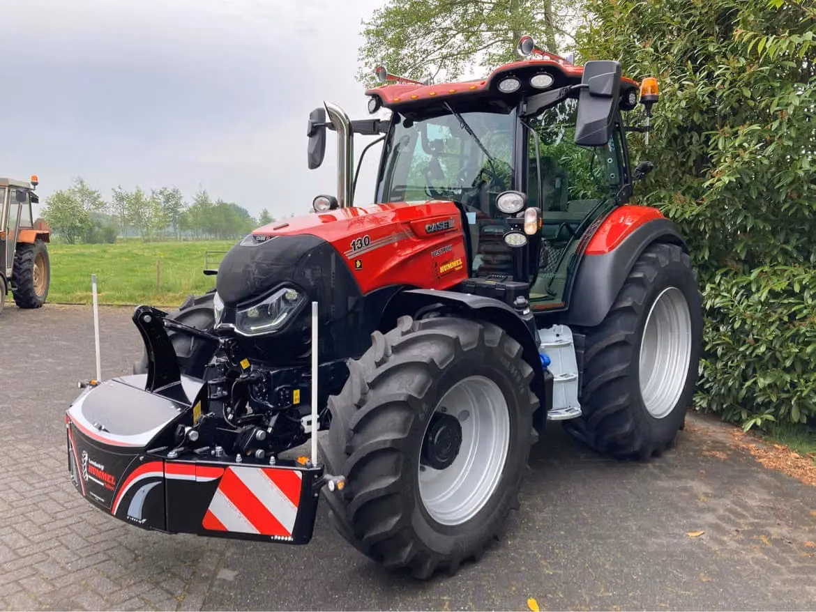 A red tractor with large tires fitted with a front weight bumper featuring reflective red and white stripes