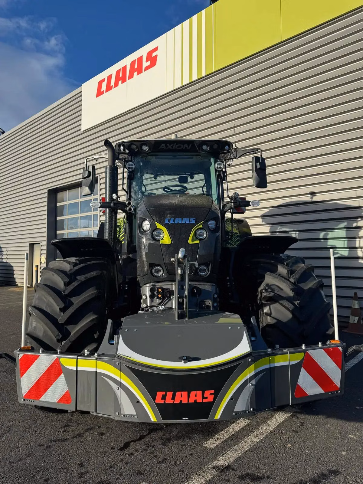 A large tractor fitted with a front weight bumper featuring red and white reflective stripes and CLAAS branding