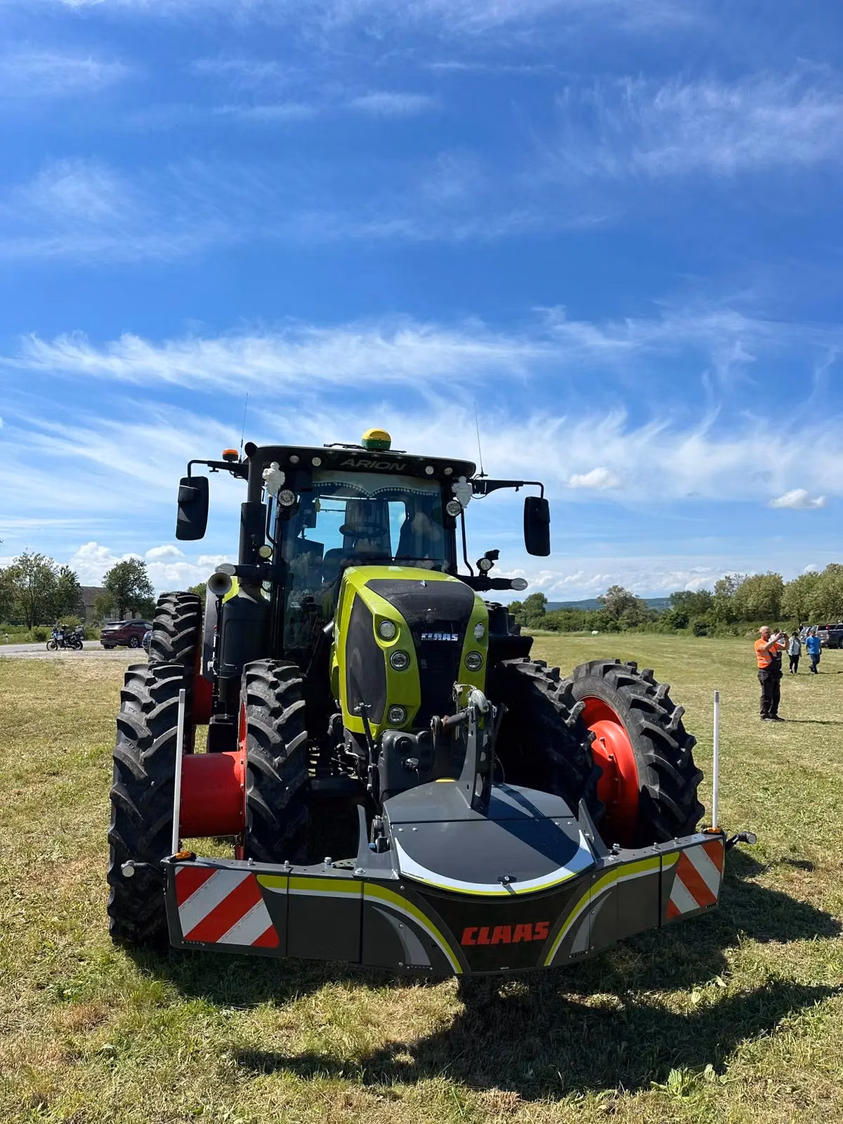 A green tractor with large tires is fitted with a front weight bumper labeled CLAAS on a grassy field