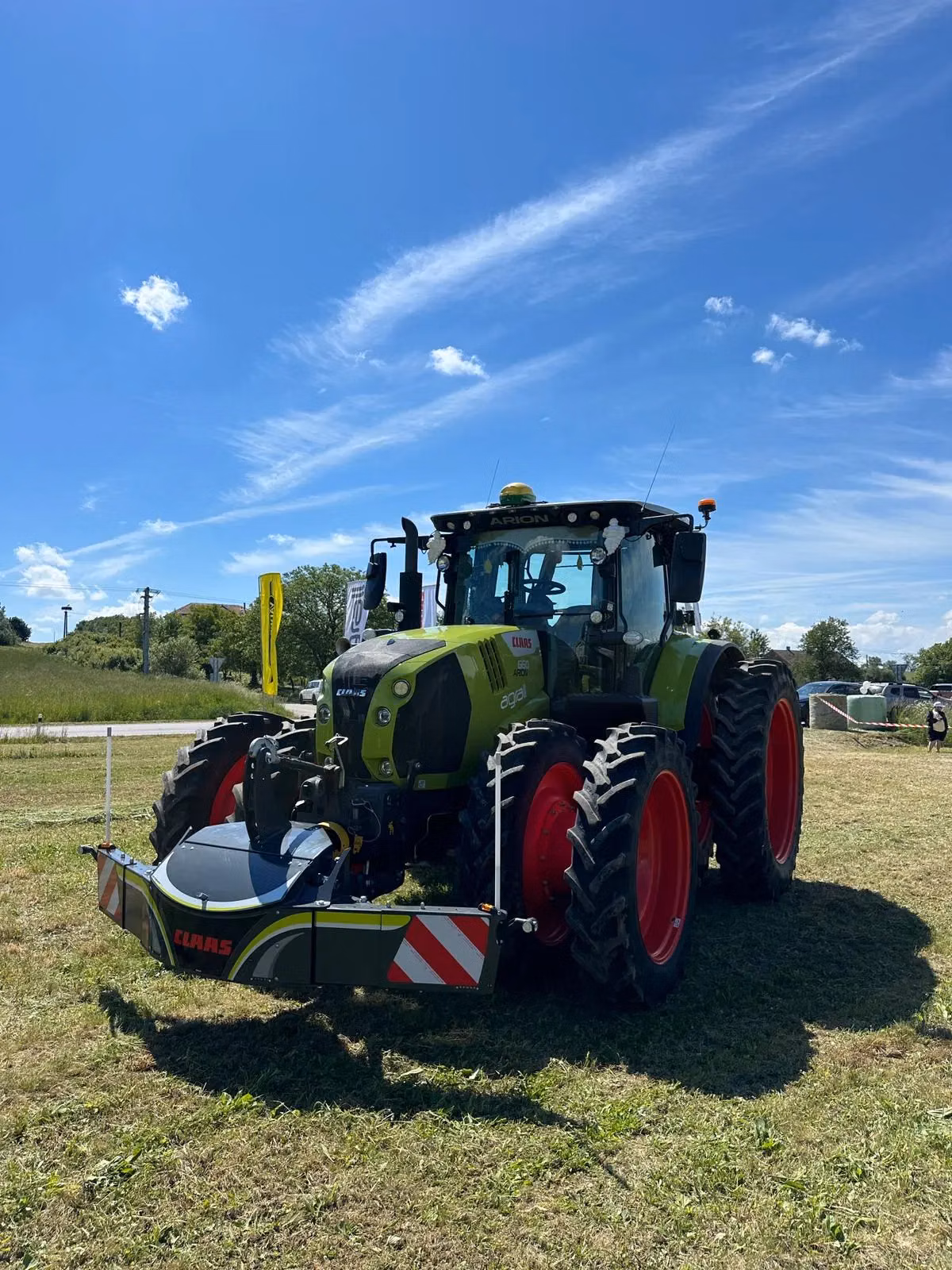 Green tractor with red wheels fitted with a front weight bumper featuring reflective stripes on grass under blue sky