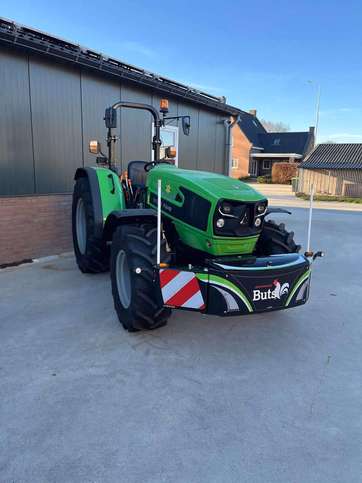 A green tractor with a black front weight bumper featuring reflective stripes and a logo, parked on concrete.