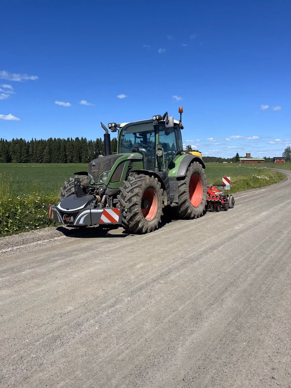 Green tractor with a front weight bumper and rear implement parked on a country road by a field under blue sky