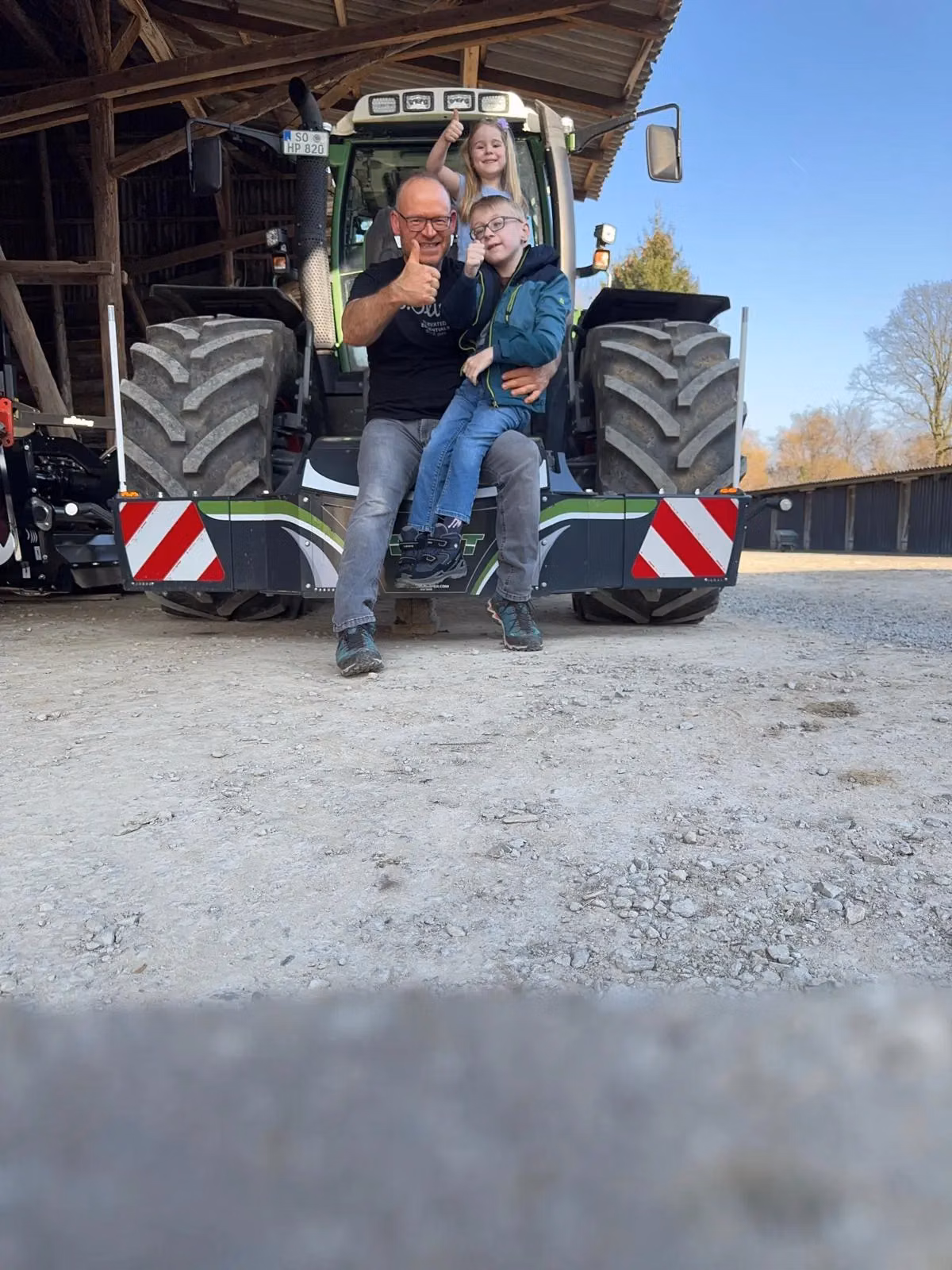 A man and two children sit on a tractor equipped with a front weight bumper with red and white stripes