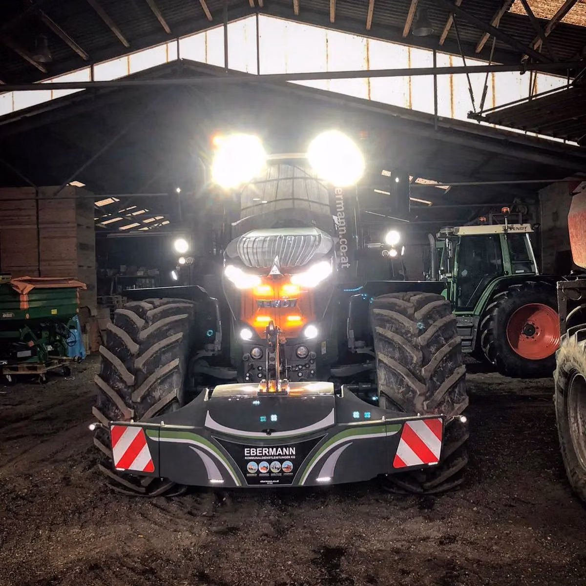 Tractor with illuminated headlights in a barn, fitted with an Ebermann front weight bumper with LED lights and reflectors