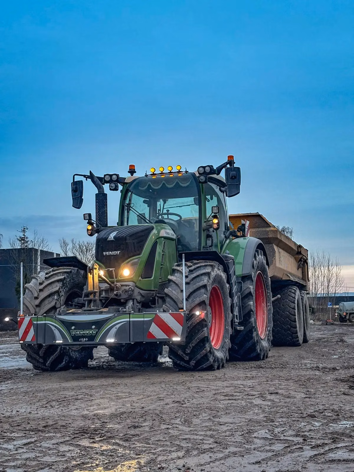 Large green tractor with a front weight bumper and visible warning stripes parked on a muddy outdoor surface