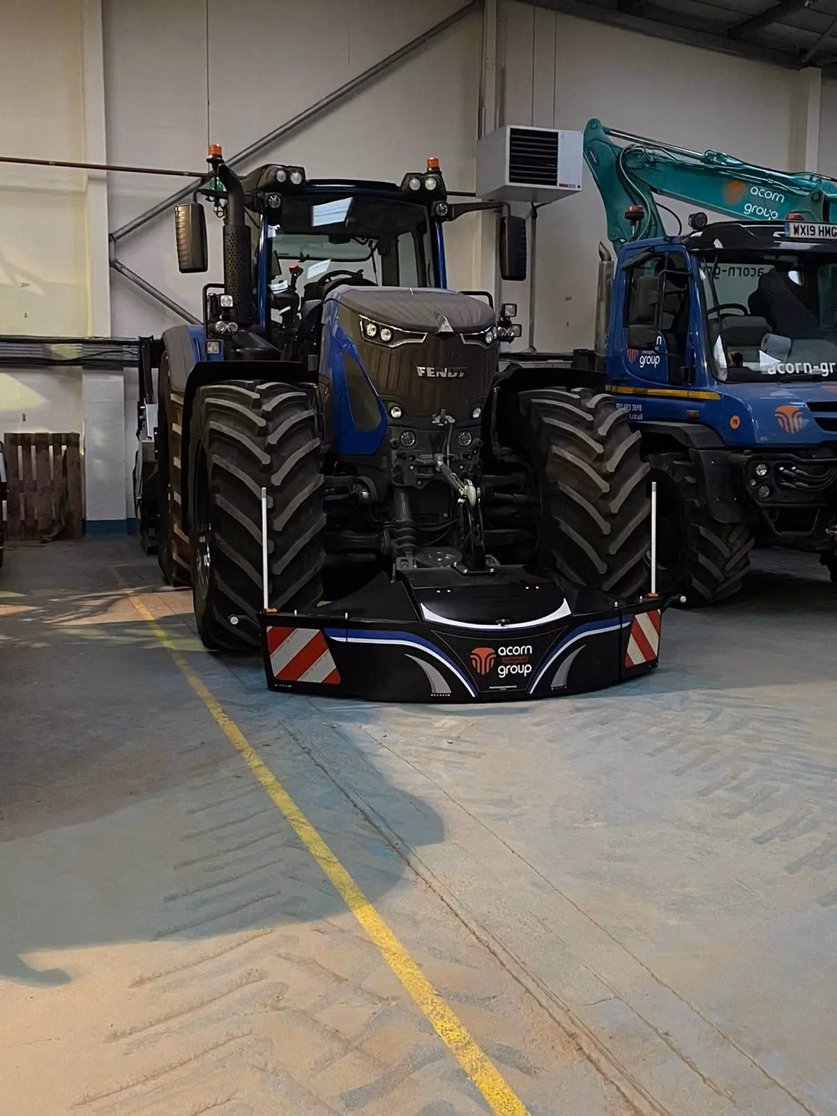 A blue tractor indoors with a front weight bumper featuring LED lighting and acorn group branding