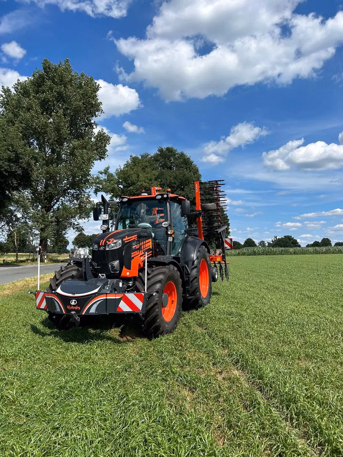 An orange and black tractor with a front weight bumper is parked on a grassy field under a blue sky with clouds