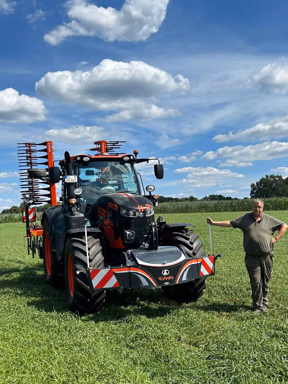 A man stands next to a Kubota tractor in a field, featuring a large front weight bumper with red and white stripes