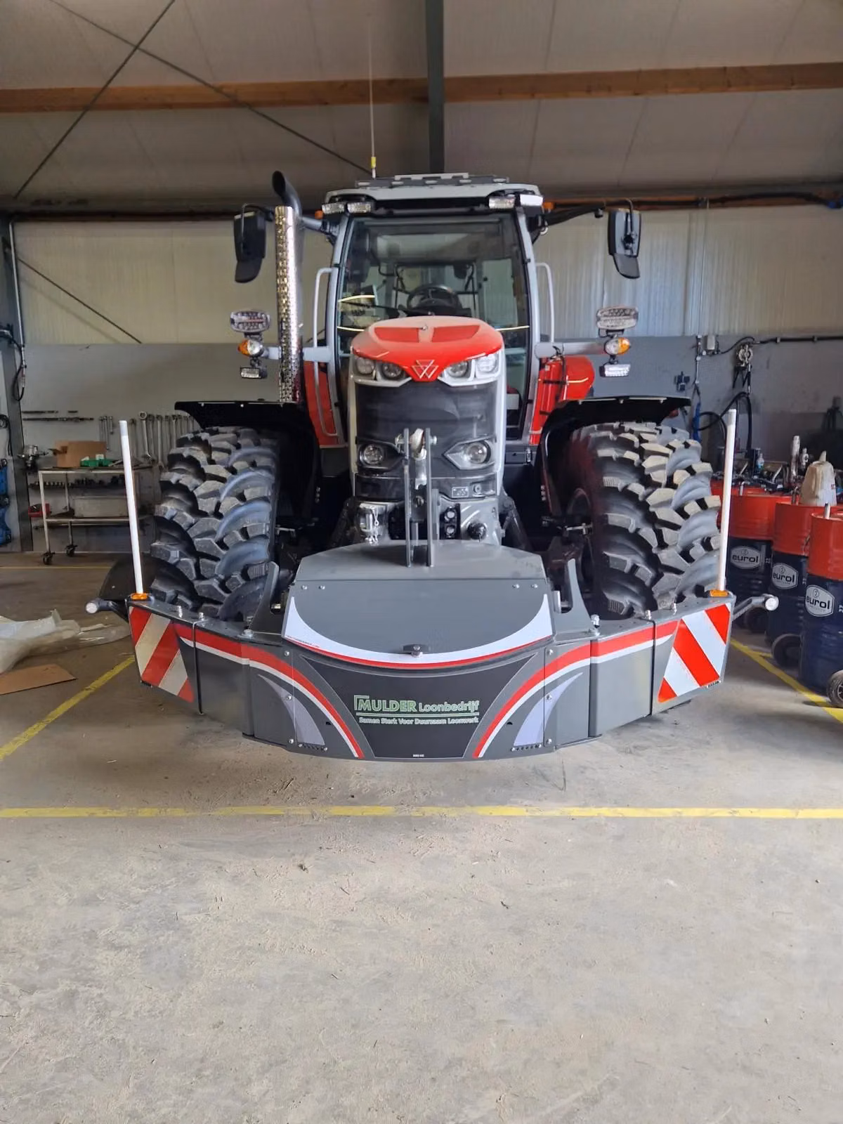 Large red and grey tractor indoors with a heavy-duty front weight bumper featuring reflective red and white markings
