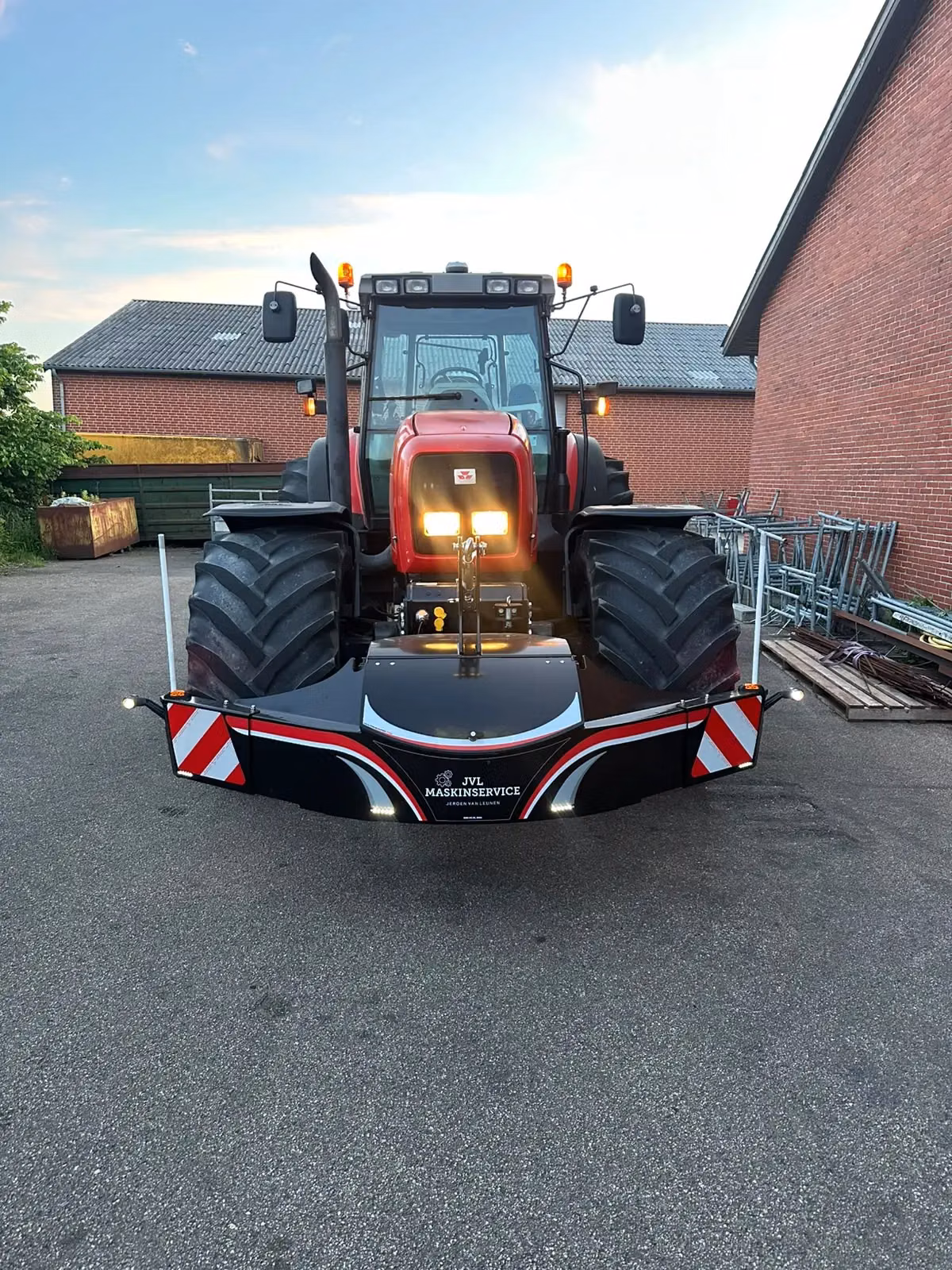 A red tractor fitted with a front weight bumper featuring LED lights, reflective stripes and JVL MASKINSERVICE branding