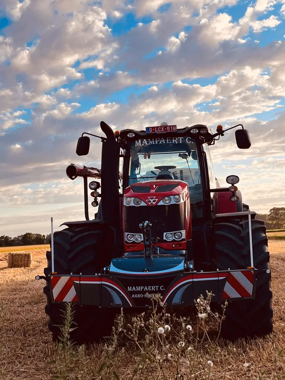 Red tractor fitted with a front weight bumper featuring reflective stripes, parked in a harvested field