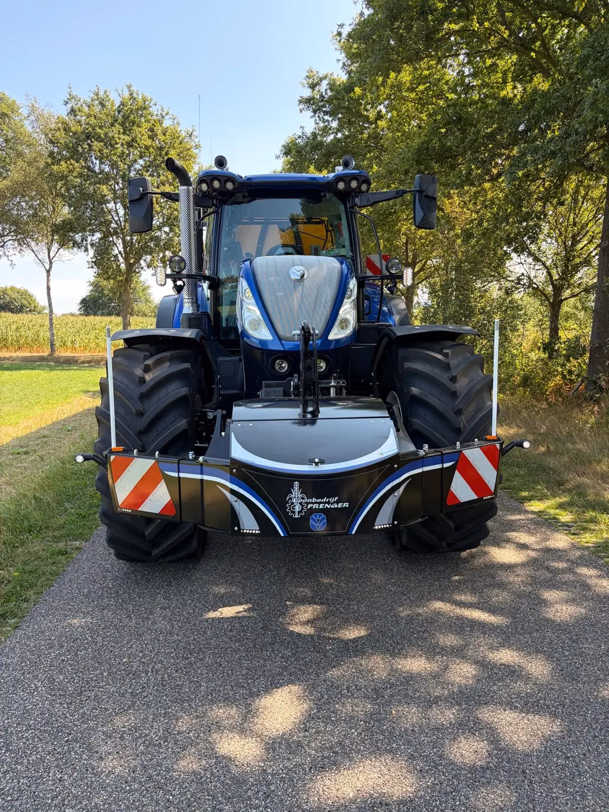A blue tractor on a rural road with a large black front weight bumper featuring reflective red and white stripes