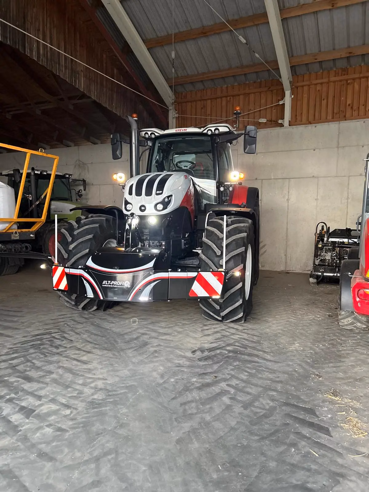 A large tractor fitted with a front weight bumper featuring red and white safety stripes parked in a shed